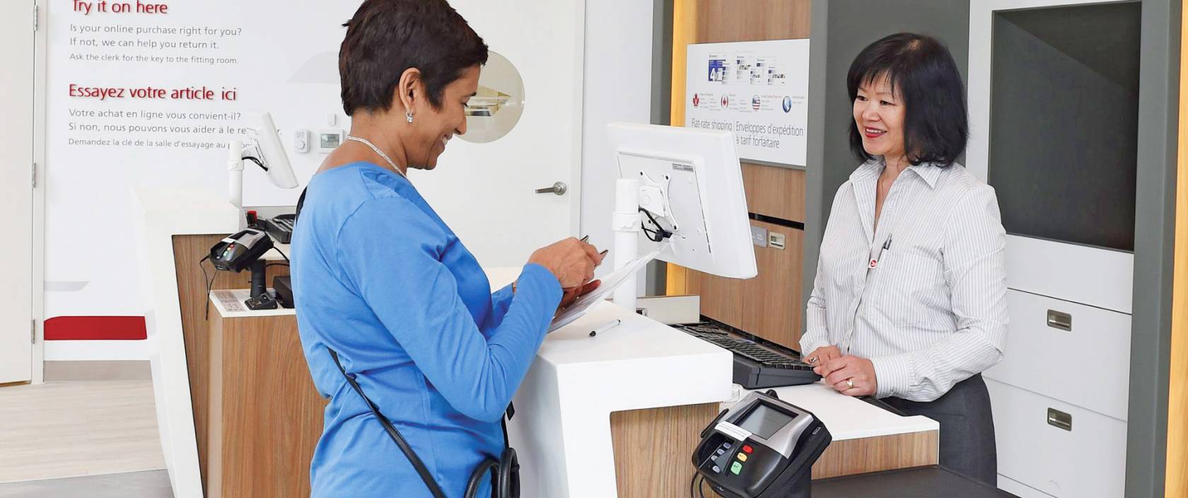 A woman completes her ID verification process at a Canada Post counter by presenting her government-issued photo ID.