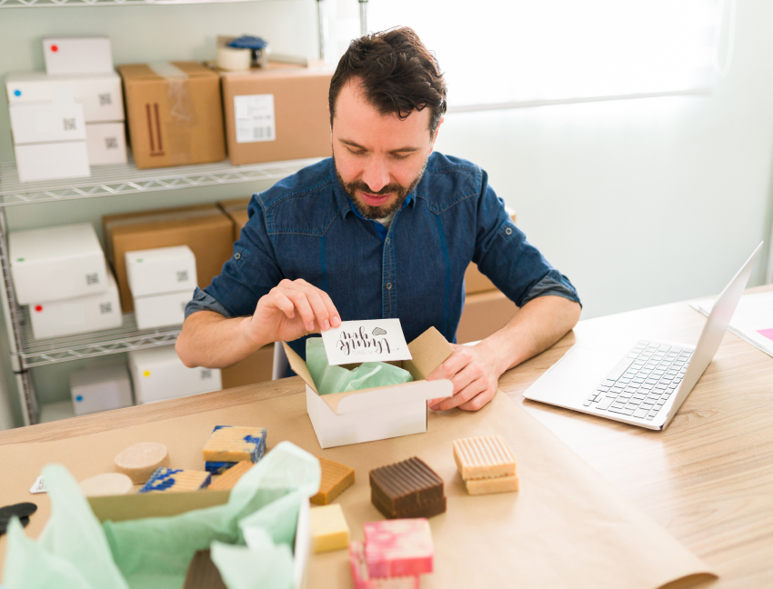 A man sits at a table and prepares a small parcel for shipping.