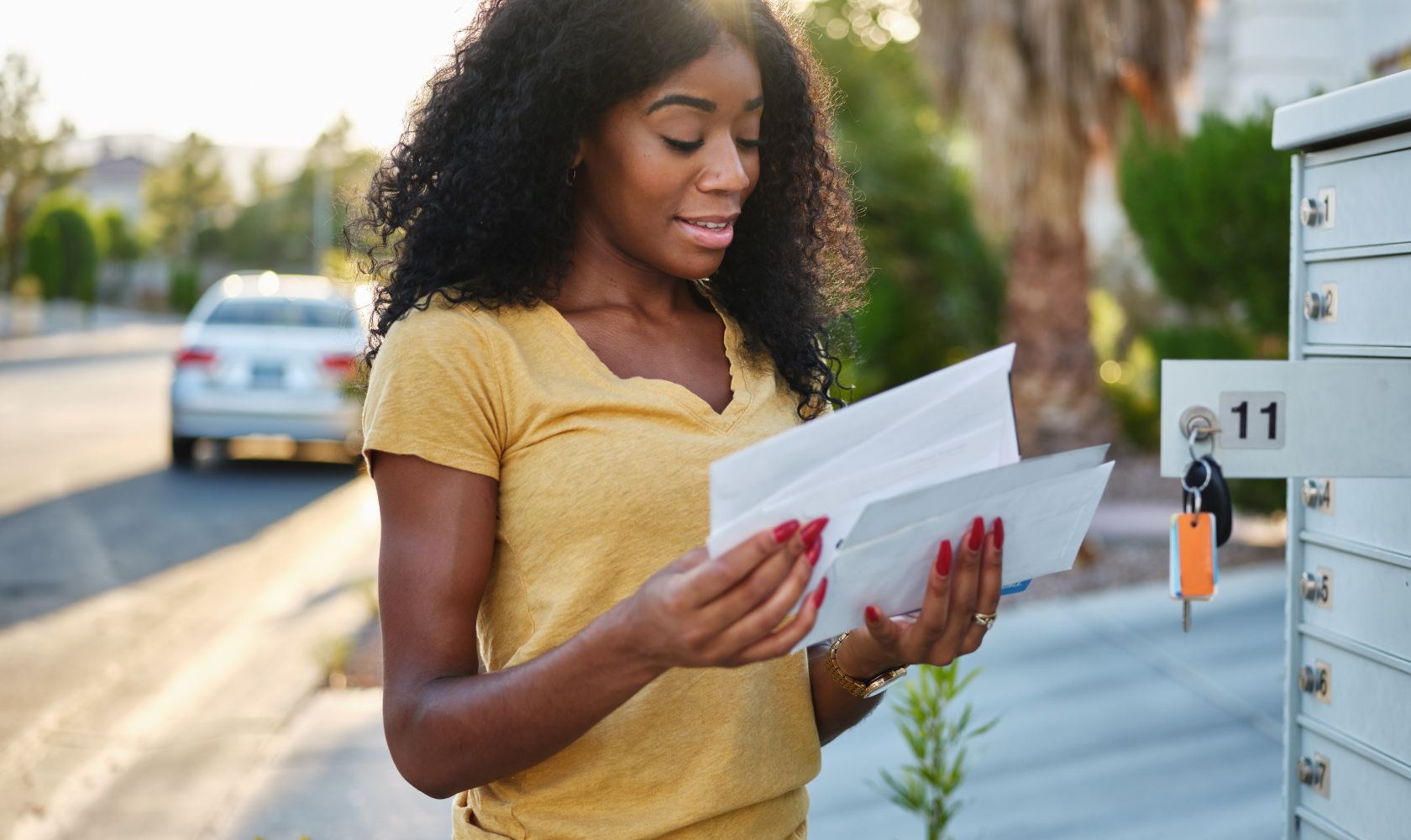 Une jeune femme aux cheveux frisés foncés vérifie son courrier à une boîte postale communautaire. 