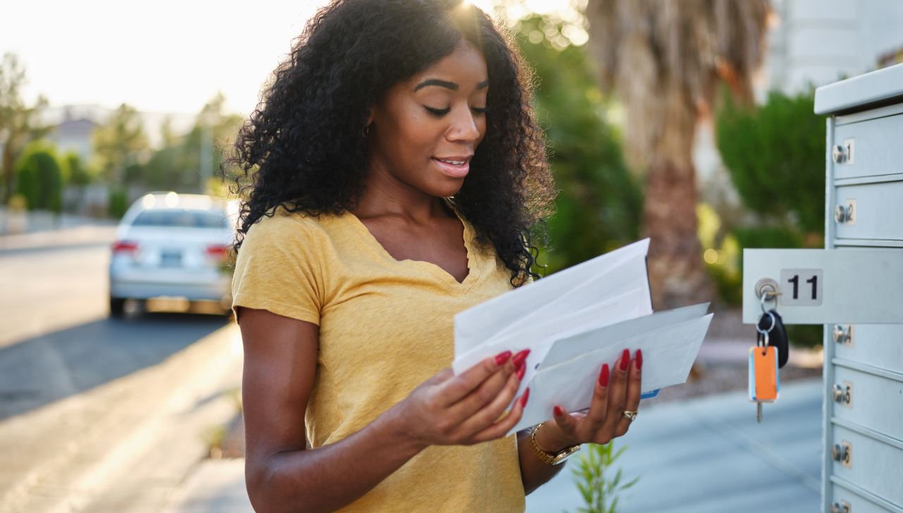 Une jeune femme aux cheveux frisés foncés vérifie son courrier à une boîte postale communautaire. 