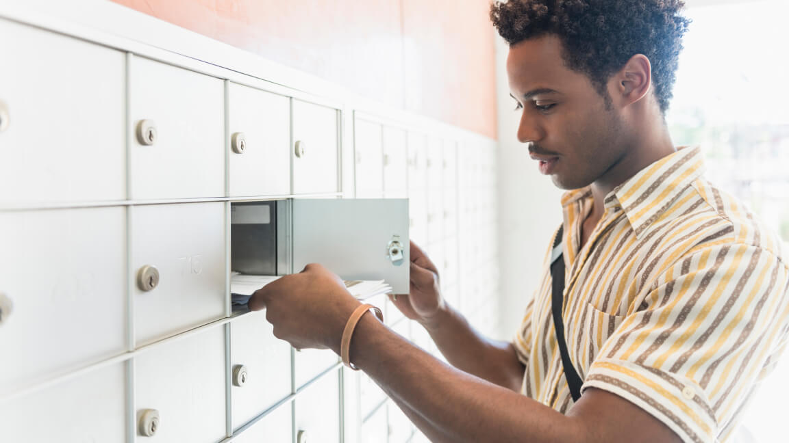 Un homme récupère du courrier dans un compartiment de boîte postale multiple dans le hall d’un immeuble d’habitation