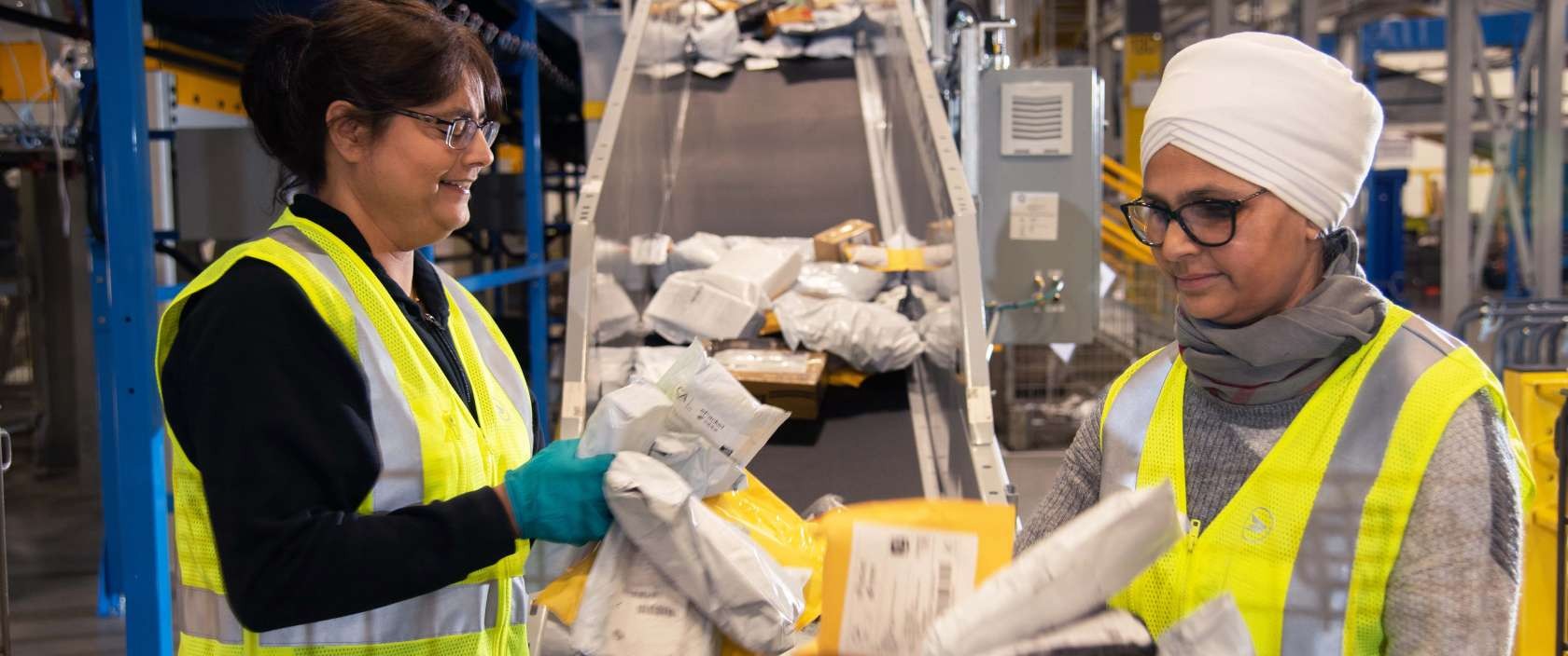 Deux employées de Postes Canada portant un gilet de sécurité jaune vif trient des colis et des enveloppes 