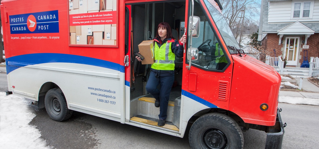 Agente de livraison sortant d’un camion de Postes Canada dansun quartier résidentiel pour livrer un colis