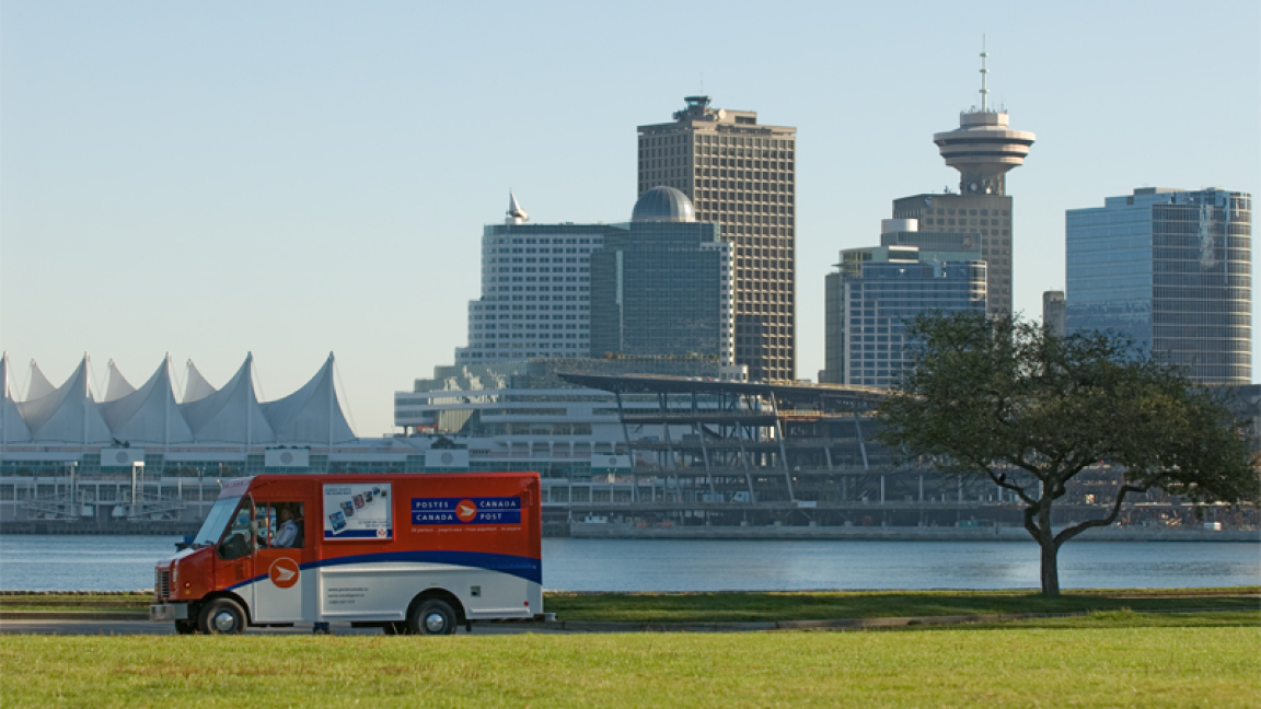 Un camion de Postes Canada circule le long de Coal Harbour et la ville de Vancouver est visible en arrière-plan.